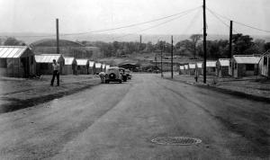 Street-level photograph of the Rendael dormitories, circa late 1940s, depicting dirt road and metal barracks; portion of Houston Field House visible in distance.