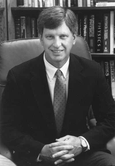 Black-and-white photograph of Jack Wilson, seated at his desk with his hands folded in his lap