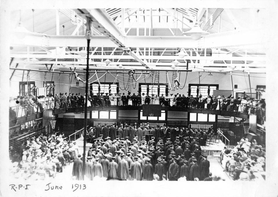 Black and white photo, taken from the back, showing the Class of 1913 in caps and gowns and the onlooking crowd